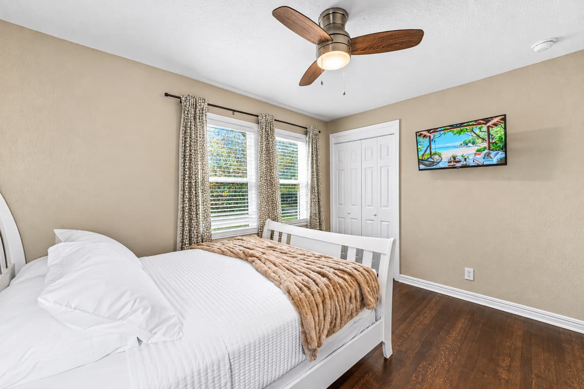 Bright bedroom featuring a comfy bed, wall-mounted TV, and large windows for a relaxing retreat.