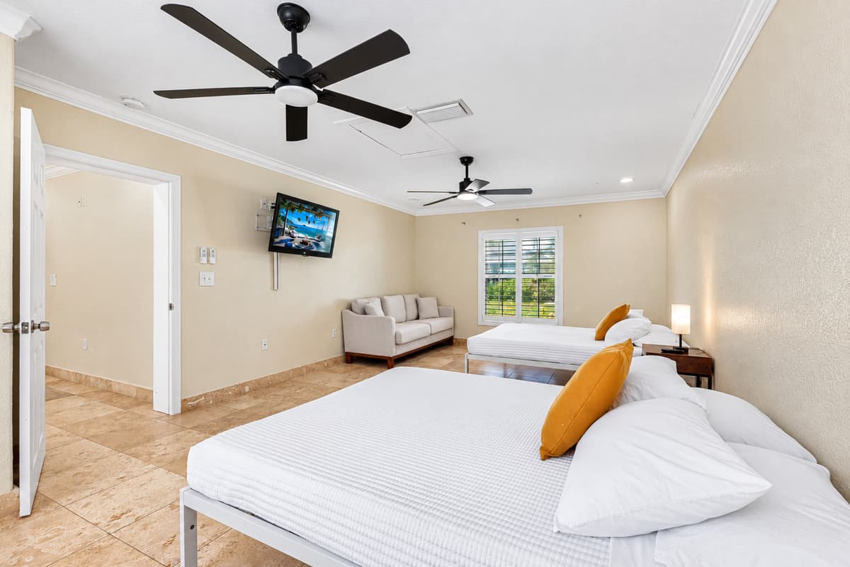 This bright and airy bedroom features two comfortable beds, a cozy sitting area, and a wall-mounted TV for ultimate relaxation.