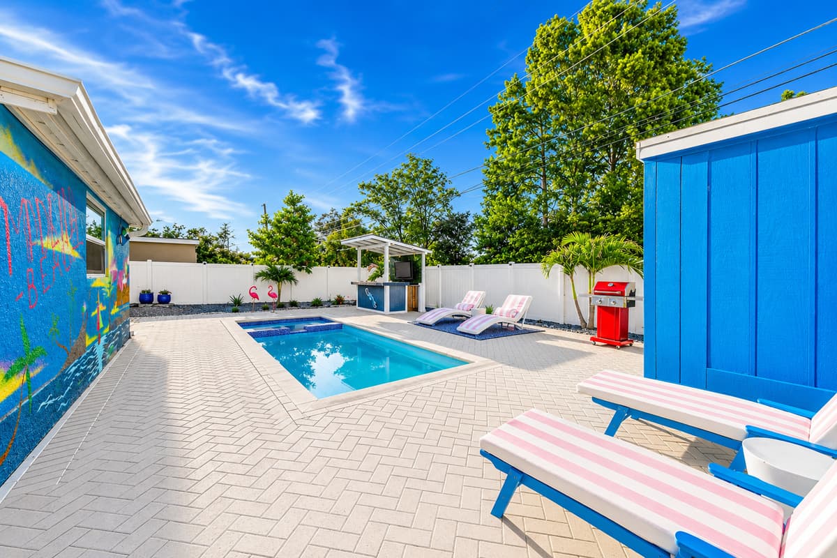 Backyard perspective highlighting the pool house, lounge seating, barbecue area, and spacious outdoor layout.