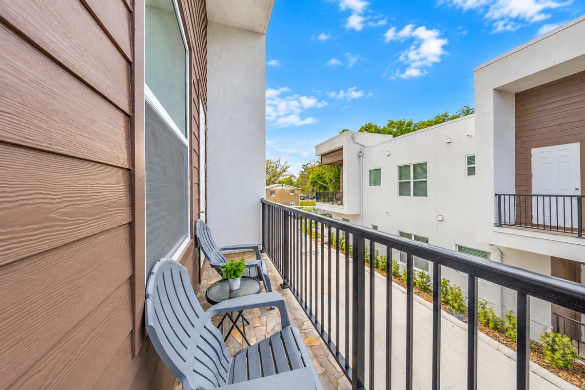 Fresh air without leaving home. A balcony with seating looks out over the courtyard and the treetops beyond. Step outside for a phone call, a quiet coffee, or a breath of warm Florida evening air.