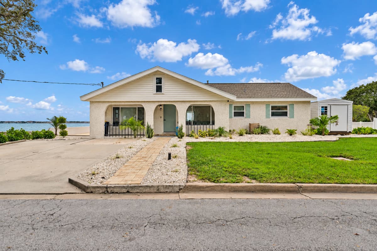 A charming coastal home from the street. A classic single-story home with an arched front porch, fresh landscaping and the bay peeking through. Simple, inviting and easy to find.