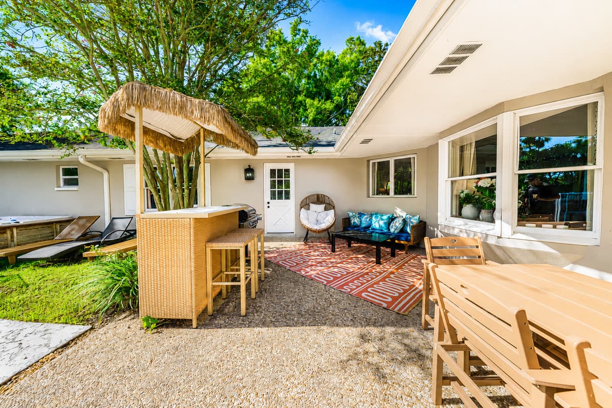 Covered patio, tiki bar, and the pool a few steps beyond. The backyard is built in zones.