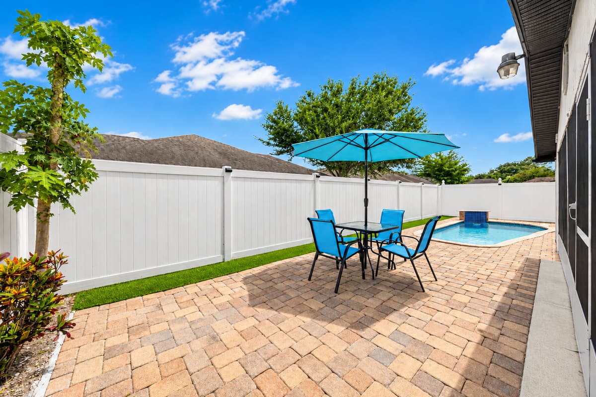 Poolside outdoor dining area featuring comfortable seating and a large umbrella, perfect for enjoying meals, morning coffee, or evening drinks under the Florida sun.