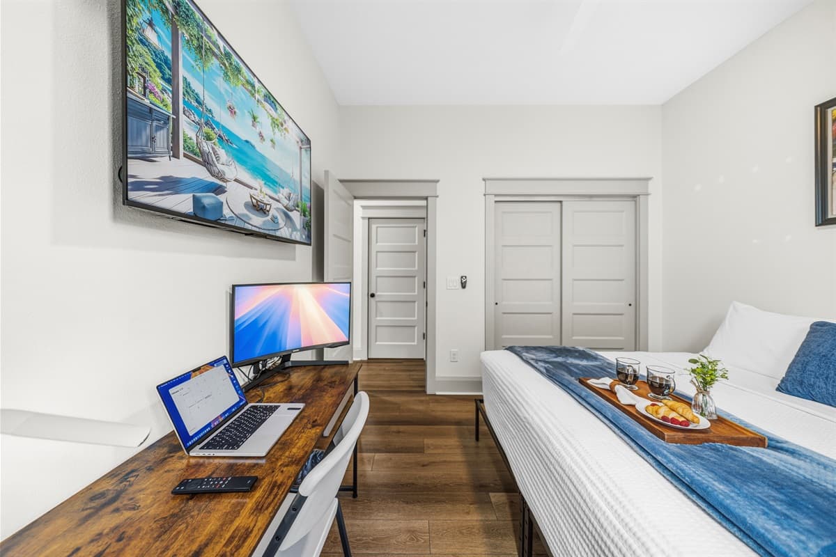 Work-from-paradise setup! This bedroom includes a smart TV, wooden desk, navy blue comforter, built-in closet, and hardwood floors. Brand-new comfort for both rest and remote work in Seminole Heights, Tampa.