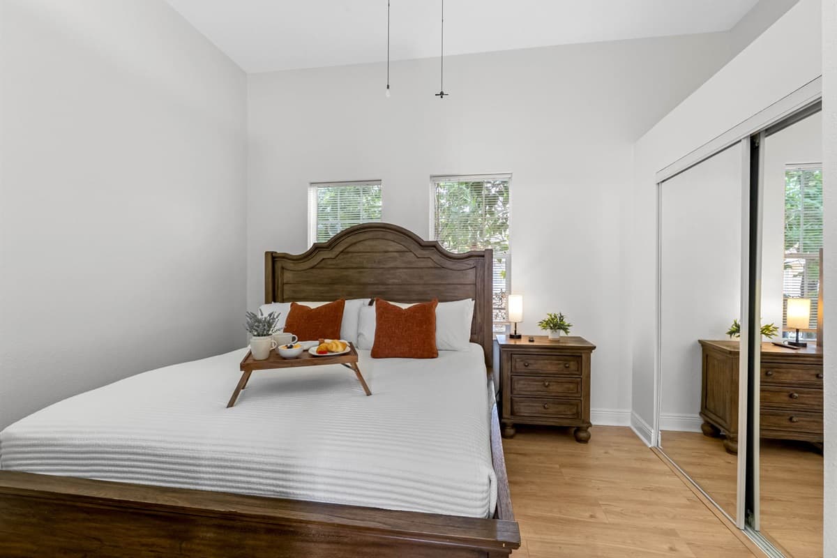Relax in this inviting bedroom featuring a warm wood bed frame, crisp white linens, and soft accent pillows, creating a calm and comfortable retreat.