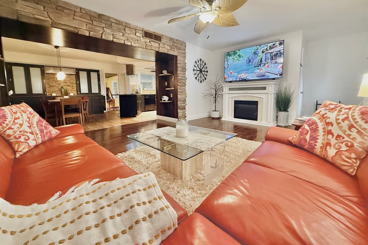 This inviting living room features a large wraparound sofa, warm wood floors, and a smart TV over a charming fireplace—perfect for movie nights or game-day lounging.