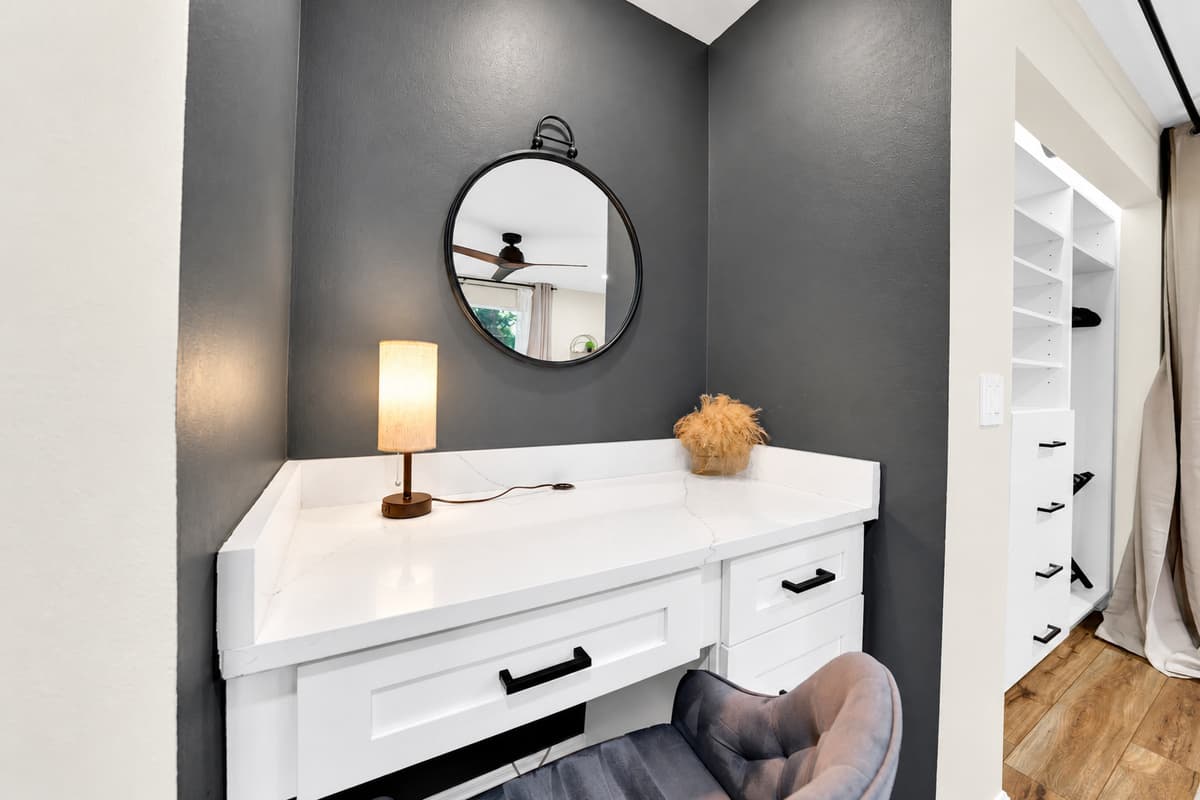 A vanity of your own, and space to use it. Wide counter, round mirror and warm lamp light, with a walk-in closet beside it — get ready without competing for mirror space with fifteen other people.