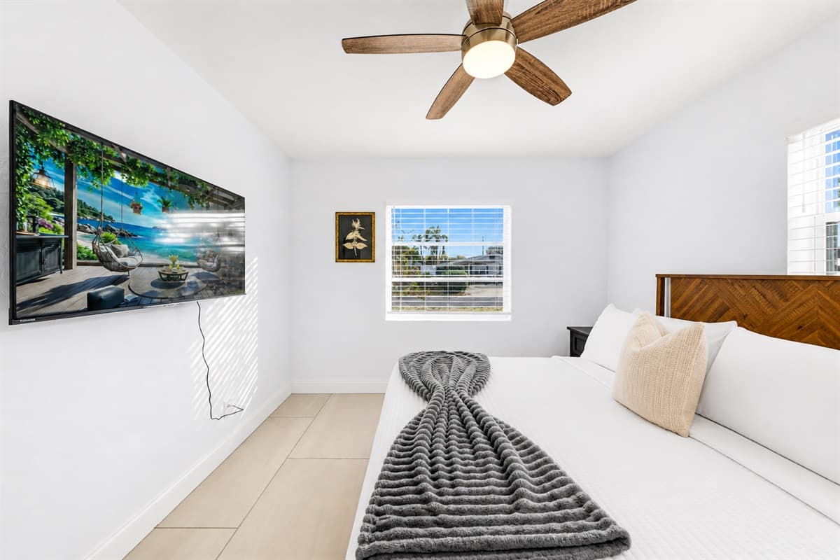 Bedroom 2 featuring a cozy queen bed, wall-mounted TV, and bright natural lighting.