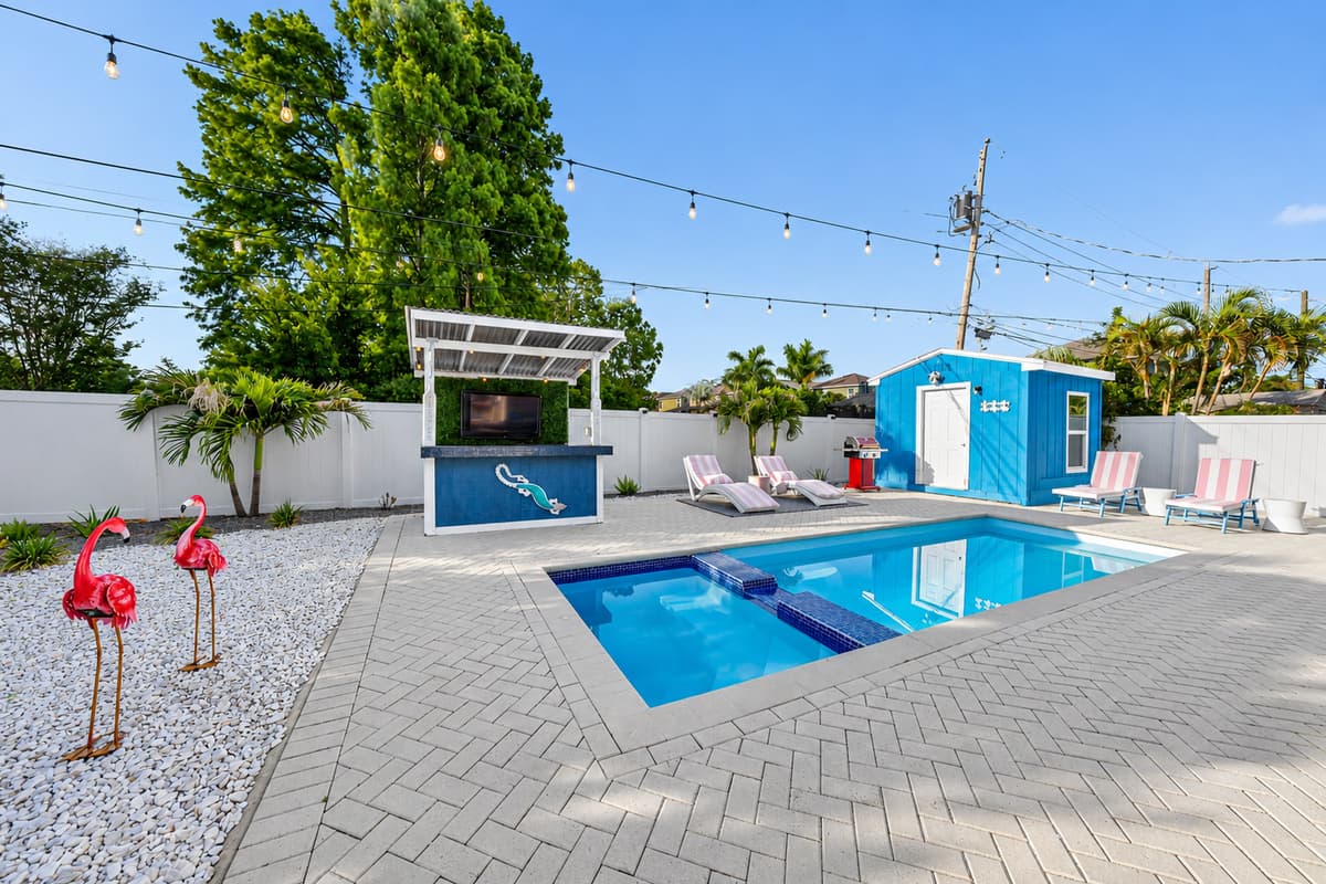 Evening-ready entertainment space featuring string lighting, outdoor TV bar, private pool, and tropical landscaping.