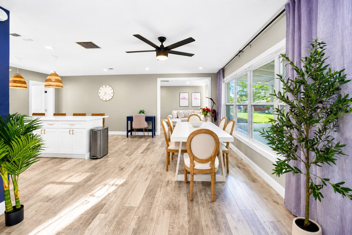 Bright open-concept dining area with large picture windows, white dining table, and seamless flow into the kitchen.