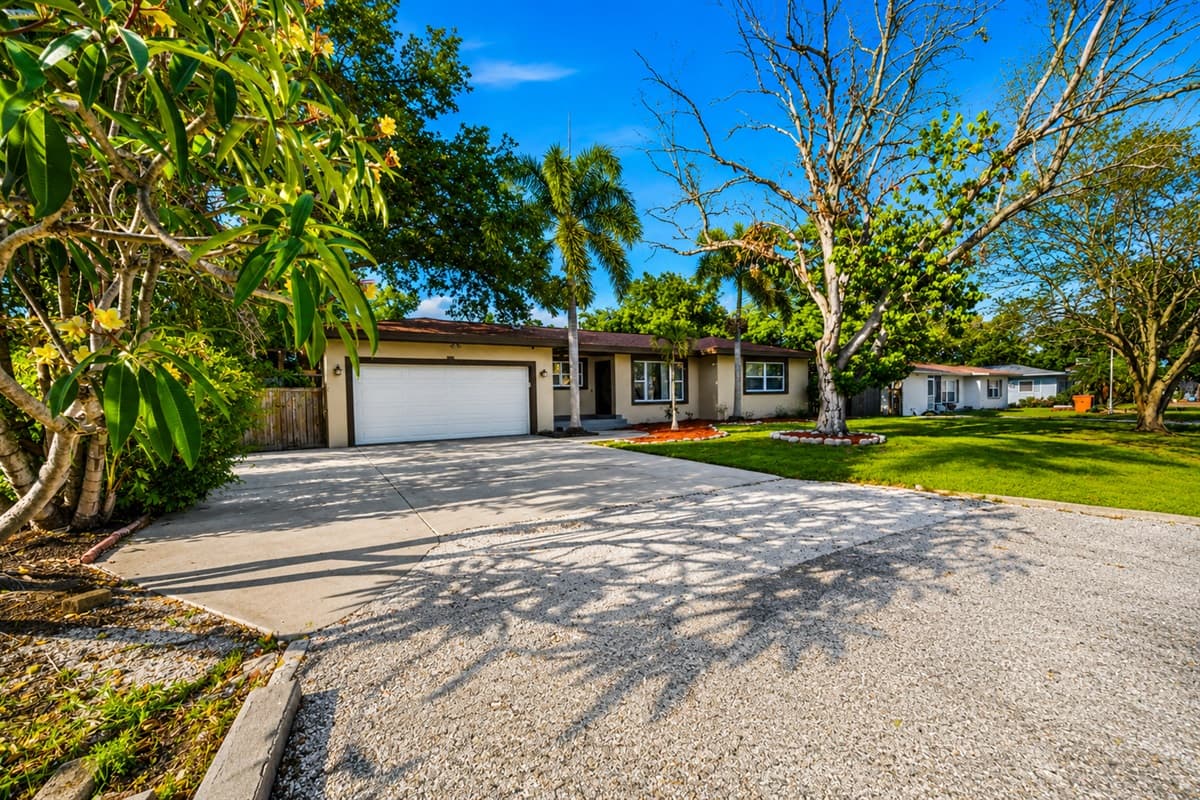 Welcoming driveway entrance framed by tropical plants and mature trees.