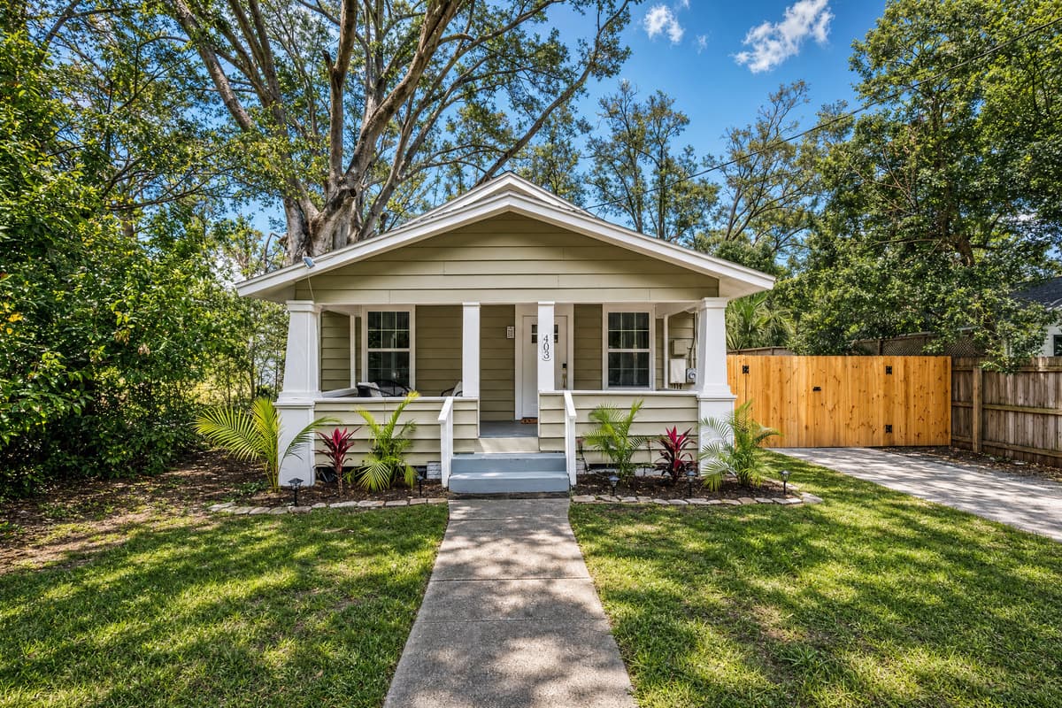 A whole detached house, not a unit carved out of something bigger. Front lawn, covered porch, a mature oak overhead, fence along the property line. What you see from the sidewalk is what you get the keys to — all of it, for your whole stay.