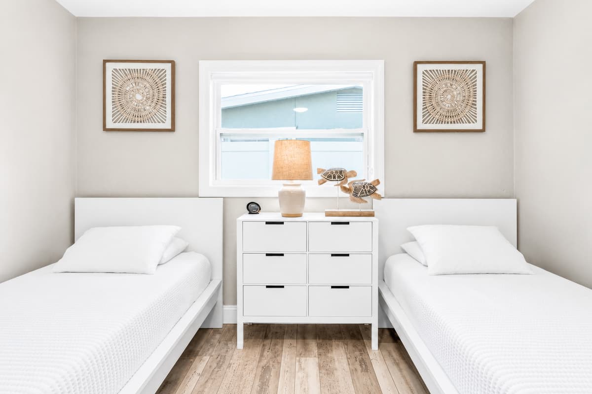 Bright guest room with two twin beds, central dresser, and warm, minimalist coastal décor.
