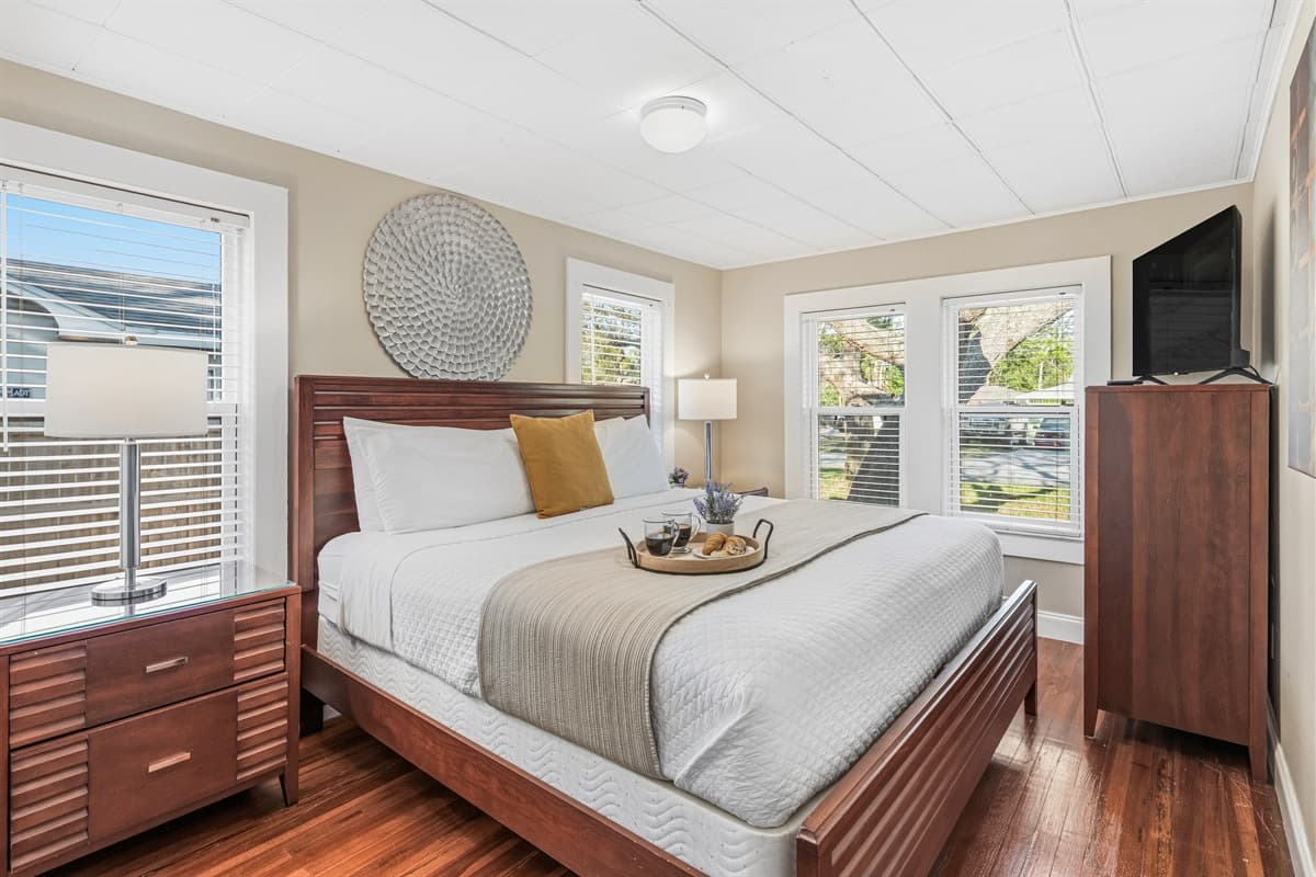 Bright bedroom with large windows, plush bedding, and a TV for entertainment.