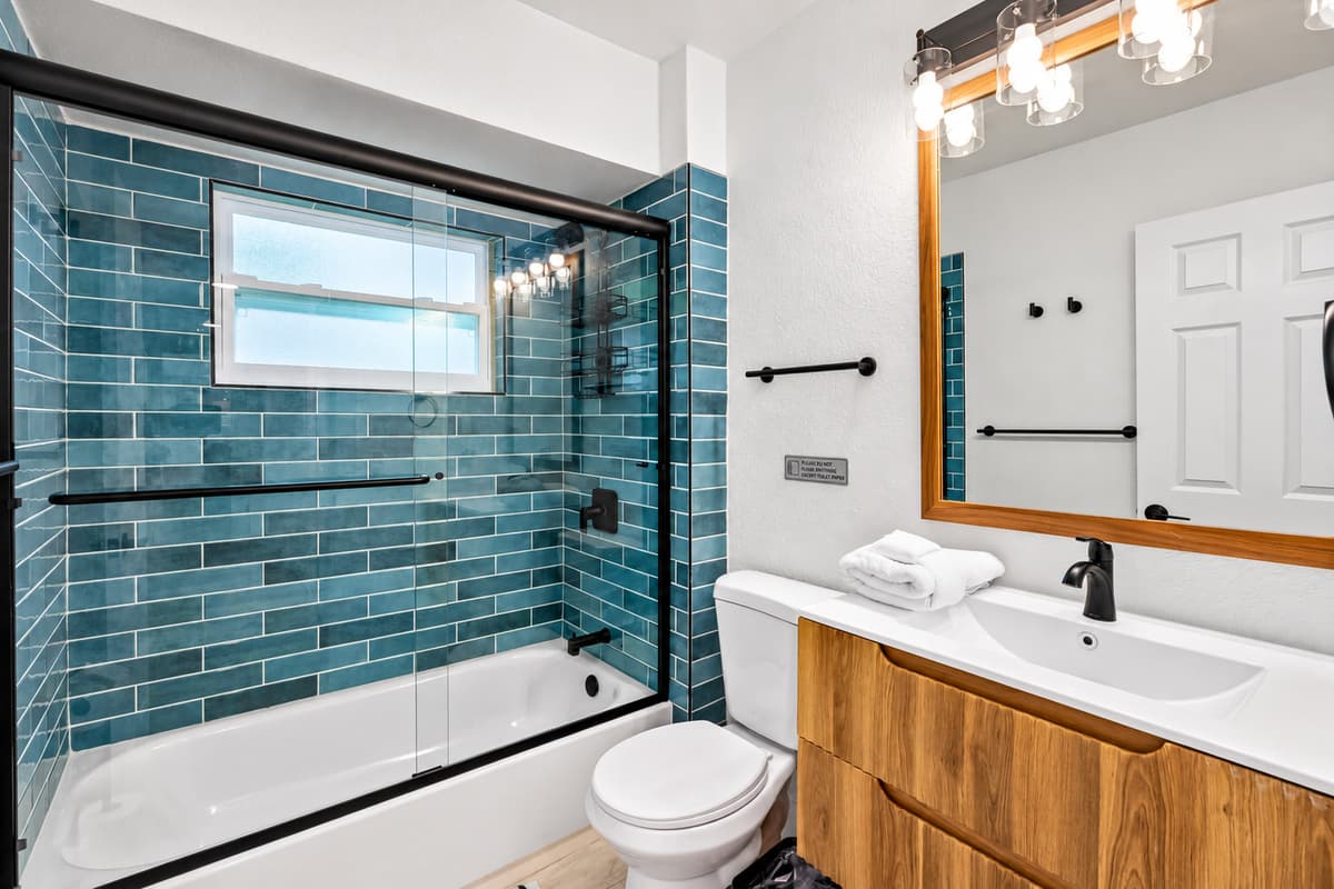 Bedroom 1 - Ensuite: Stylish and sleek, this bathroom features a stunning teal-tiled tub/shower combo, modern matte black fixtures, and a warm wood vanity for a spa-like touch.