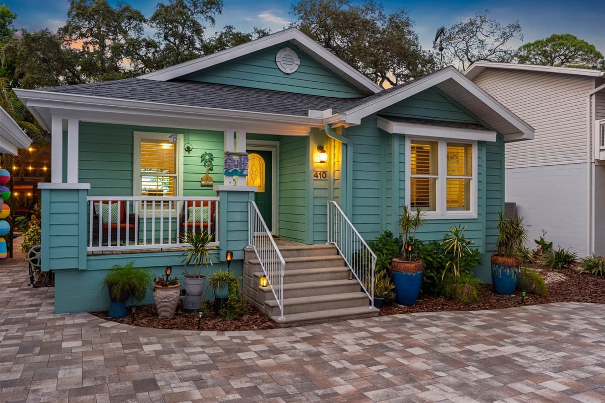 The home’s exterior radiates charm with its pastel hues, curated plants, and inviting steps leading to the front door.