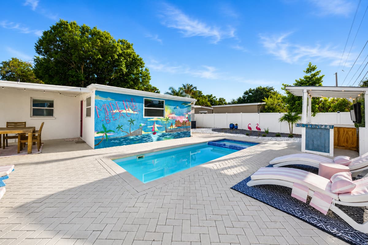 Expansive backyard featuring a sparkling private pool, tanning ledge, outdoor dining area, and tropical mural backdrop.