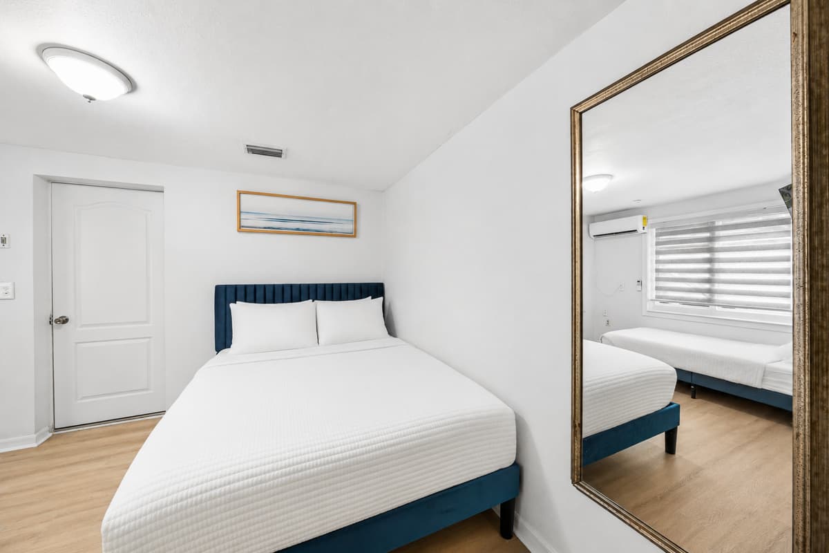 Bright and inviting guest bedroom featuring a comfortable queen bed, stylish furnishings, and a large mirror that enhances the spacious feel of the room.