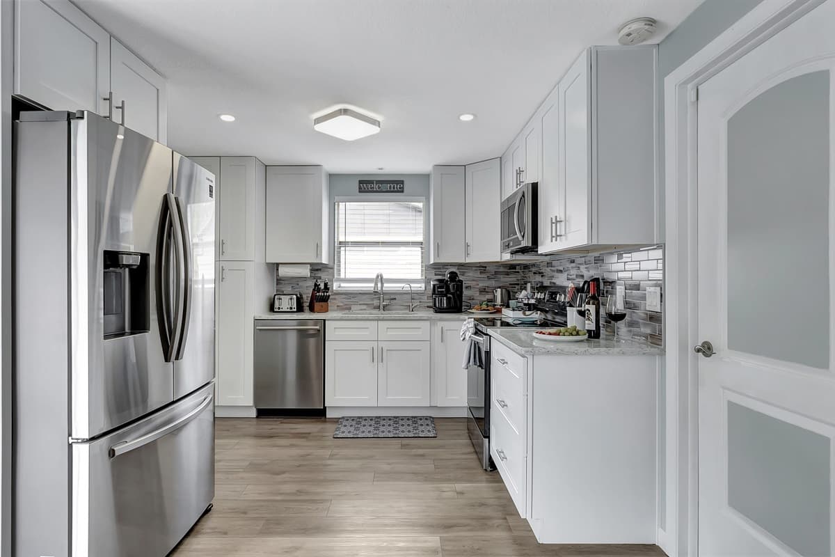 Immaculate white cupboards adorn the walls, complemented by the sleek sophistication of black and stainless finish appliances.