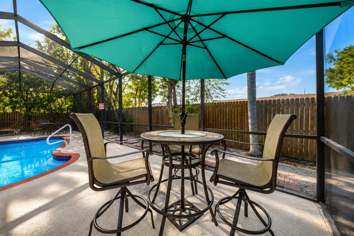 Outdoor dining space with umbrella seating overlooking the screened pool area.