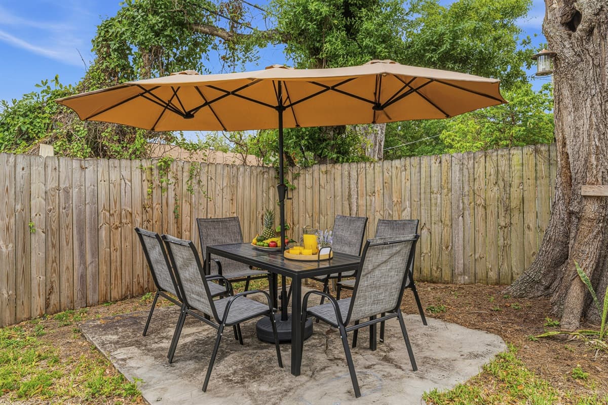 Private backyard patio featuring outdoor dining, umbrella shade, and fenced yard—ideal for meals or evening relaxation.