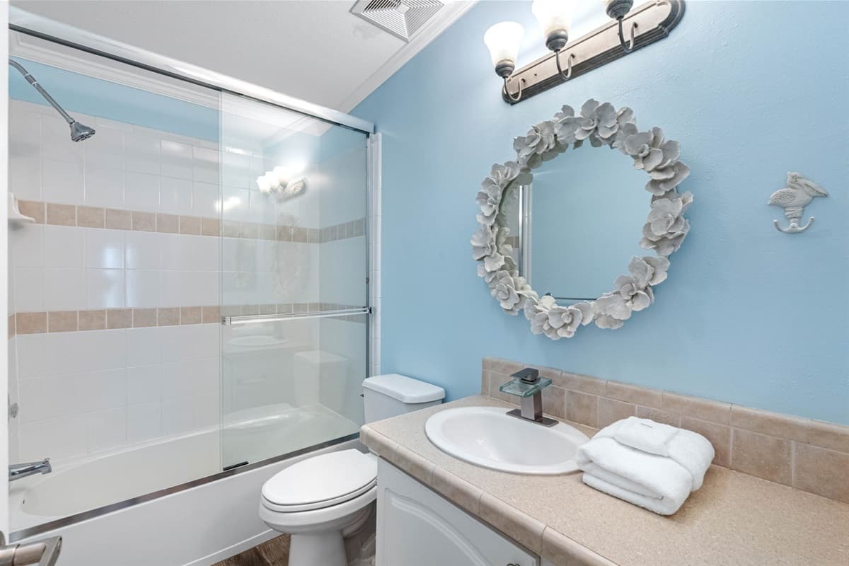 Enjoy a refreshing start to your day in this beautifully maintained bathroom, complete with a full shower and tub, stylish beige tile accents, and a unique flower-framed mirror that adds a touch of personality.