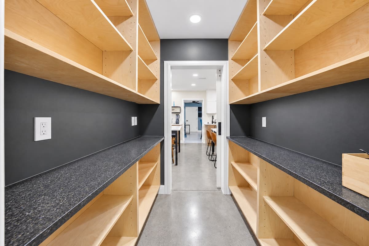 Walk-in pantry, stocked for sixteen. Floor-to-ceiling shelving on both sides with counter space in the middle — bring a week of groceries and put every single thing away properly.