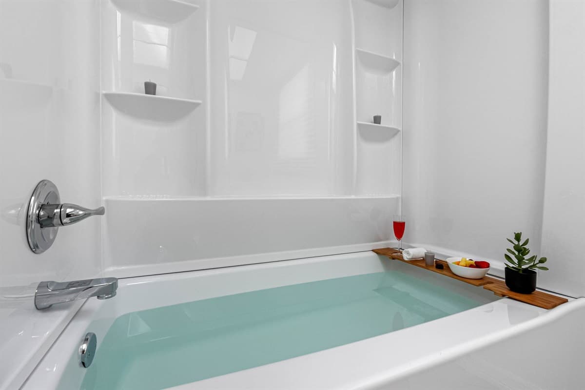 Indulge in a tranquil soak in this deep soaking tub, surrounded by a sleek, all-white surround and calming accents like candles, greenery, and a bamboo bath tray for your wine and snacks.