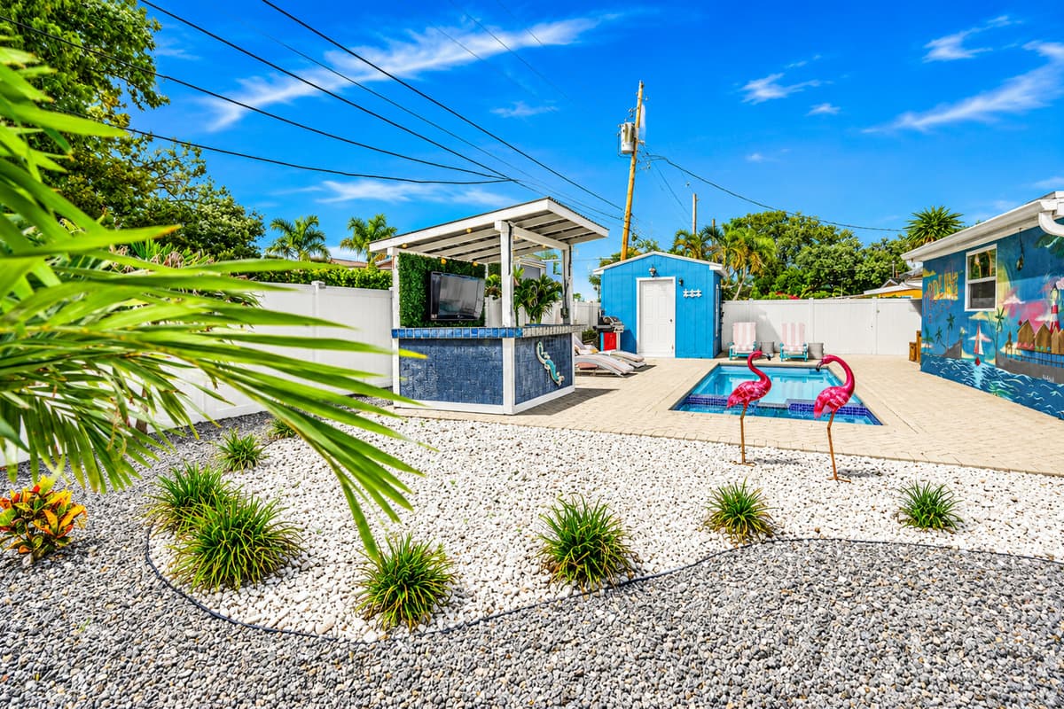 Landscaped backyard entrance view featuring decorative flamingos, tropical plants, and the resort-style pool area beyond.
