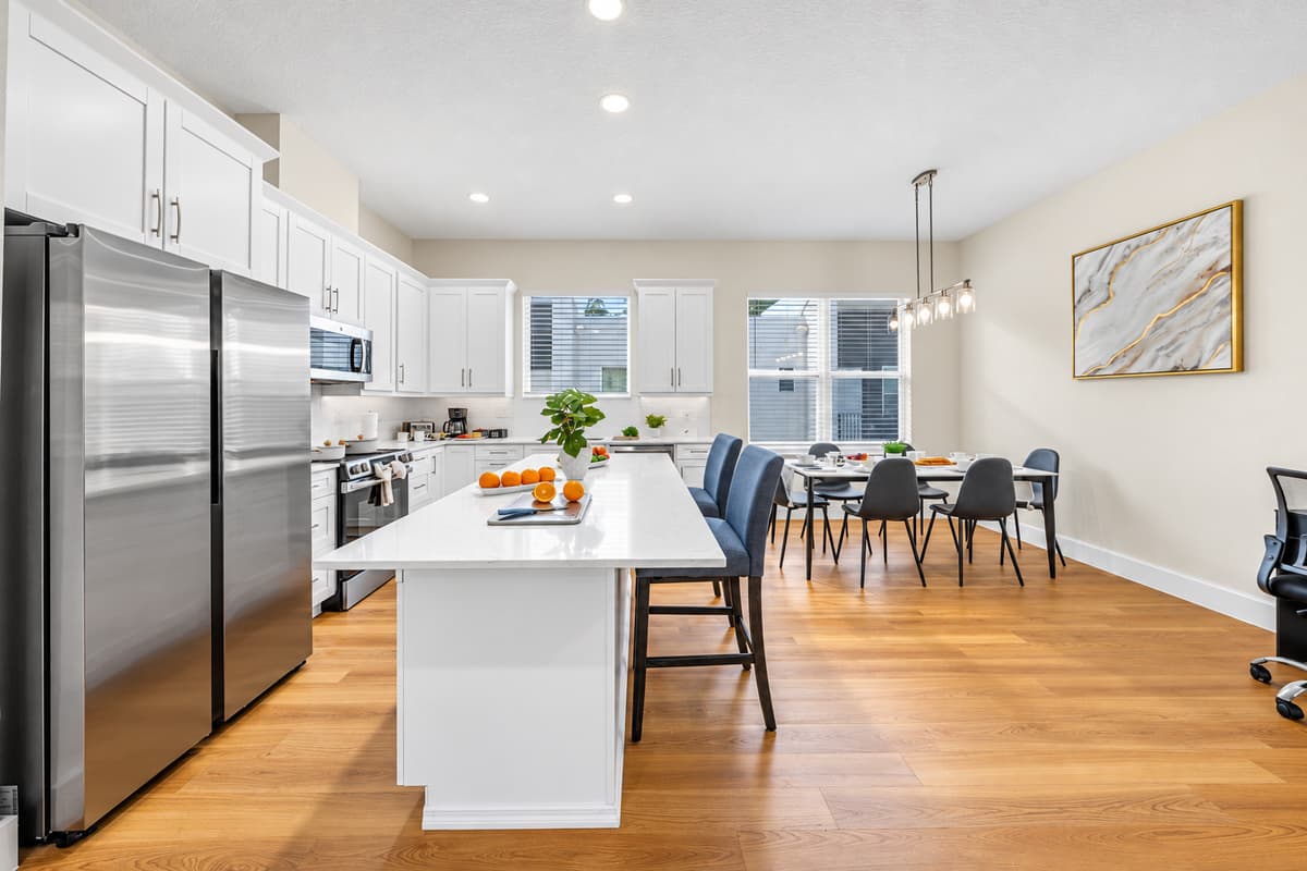 Big fridge, big island, big group meals. A full-size stainless fridge holds groceries for everyone, and the long island gives several cooks room to work. The dining table waits just past it, so plates go from stove to table in seconds.