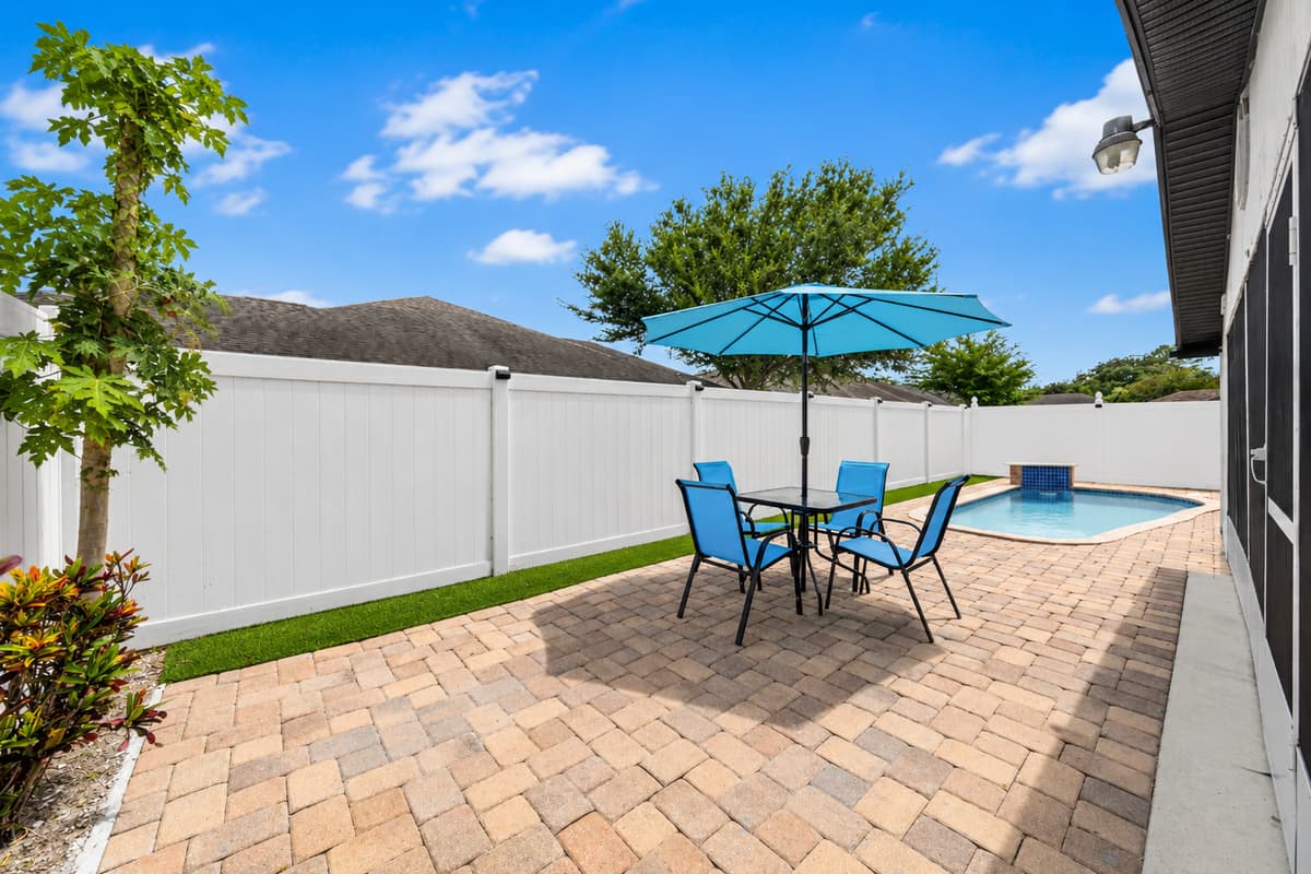 Poolside outdoor dining area featuring comfortable seating and a large umbrella, perfect for enjoying meals, morning coffee, or evening drinks under the Florida sun.