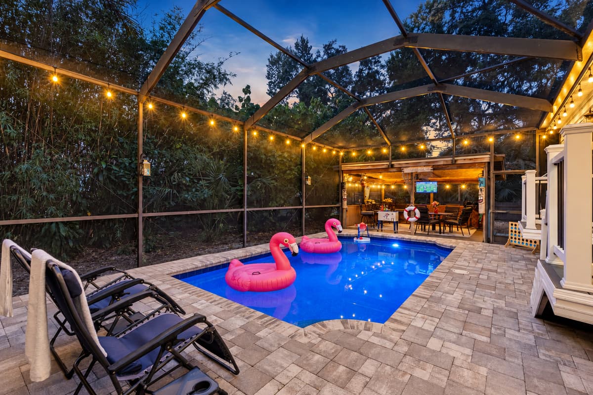 This well-designed pool area includes a spacious deck, cozy seating, and a beautiful natural backdrop behind the screened enclosure.