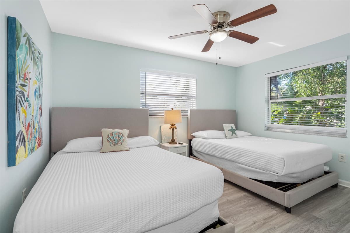 The room’s layout is both functional and inviting, offering plenty of space to relax and unwind. A nightstand with soft lighting sits between the beds.