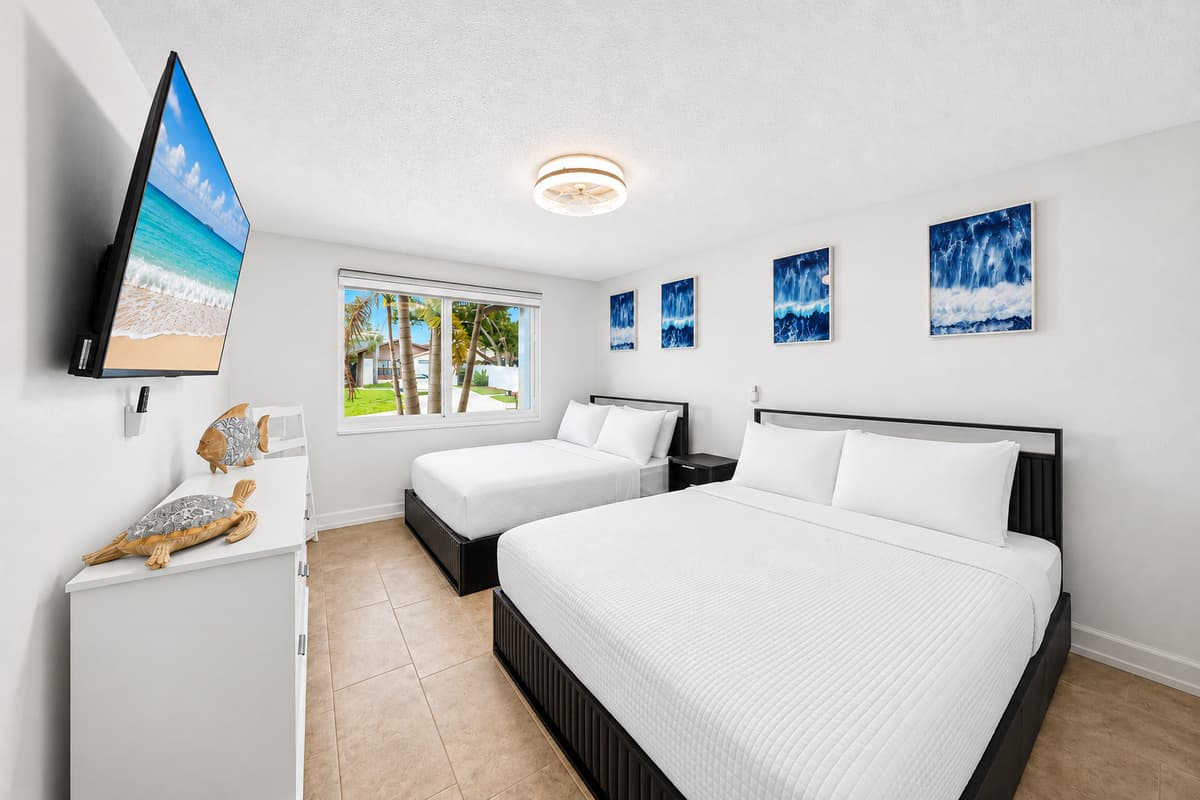 Spacious bedroom featuring a comfortable king bed, a queen bed, a wall-mounted Smart TV, and plenty of natural light for a relaxing stay.