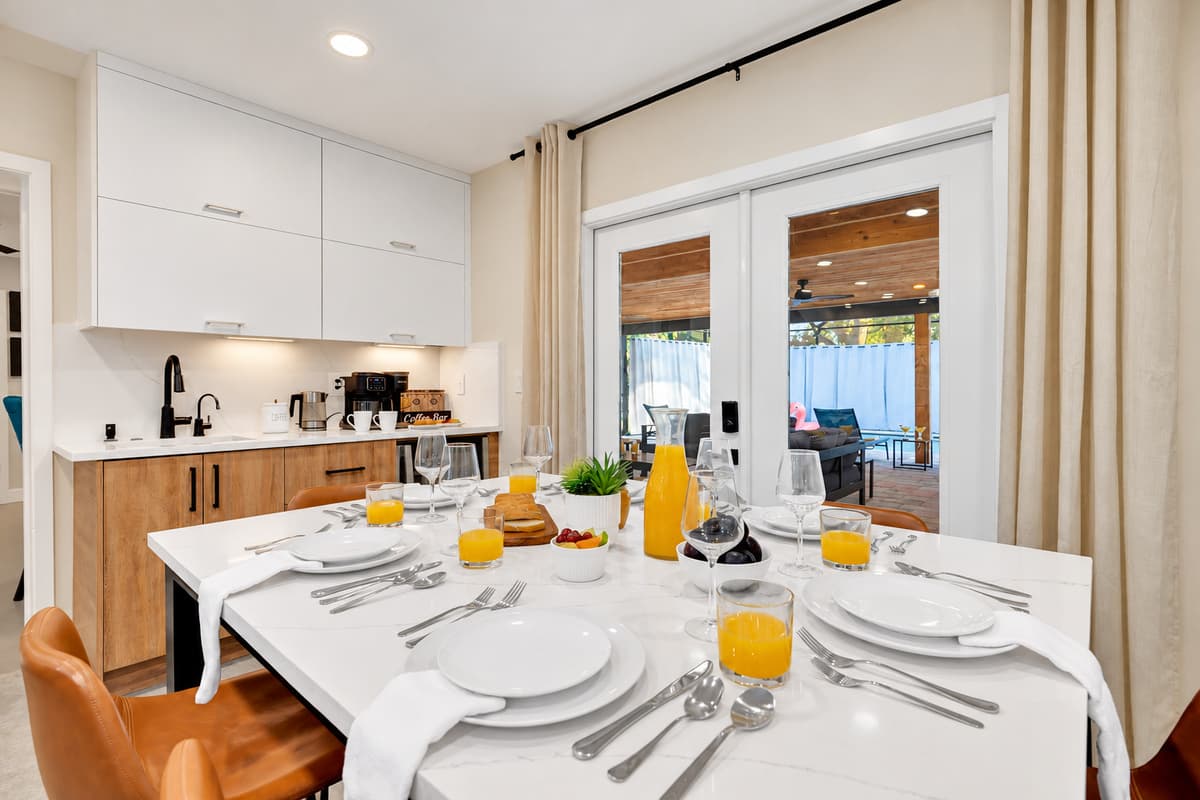 Dinner inside, pool lights outside the glass. Places set at the island with French doors onto the lanai — eat, then step straight out for a swim before bed.
