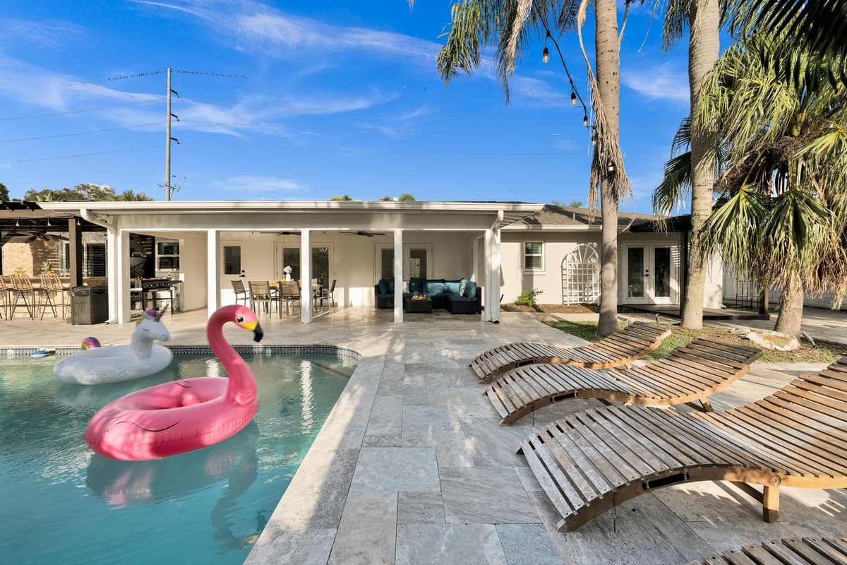 Sparkling pool with flamingo and unicorn floats, sun loungers waiting, and a fully covered lanai beyond, an instant resort escape