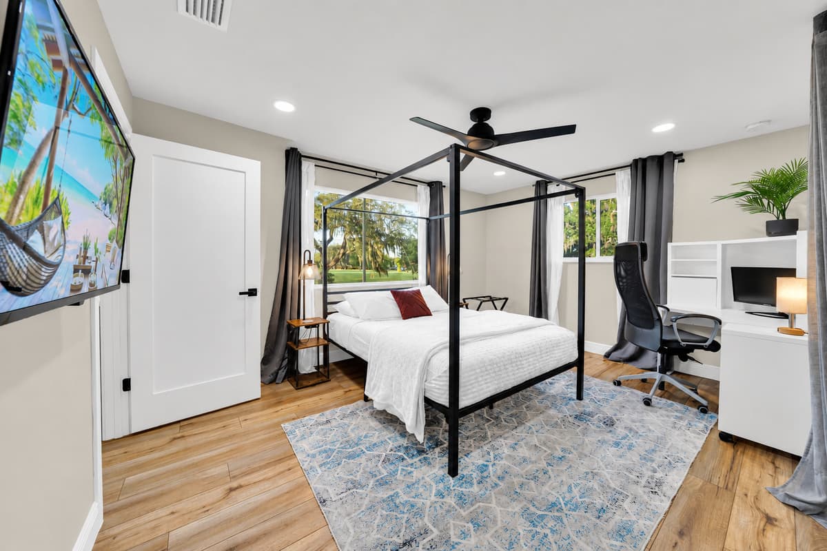 Canopy bed, private desk, door closed. Bright, high-ceilinged and quietly the best-appointed room in the house — a full workspace on one side, a proper king to sleep in on the other.