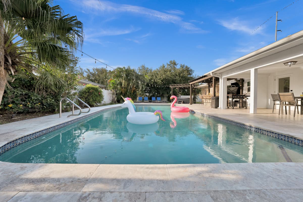 Wooden loungers lead straight to the pool where flamingo and unicorn floats bob lazily, palm trees framing a true tropical retreat.