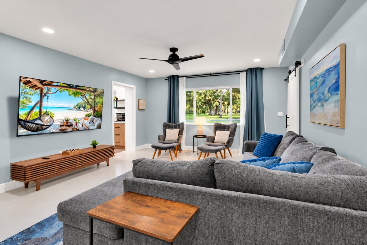 Windows on two sides, seats for everyone. Bright, high-ceilinged living space with a huge sectional and armchairs — room for the whole group without anyone perching on an arm.