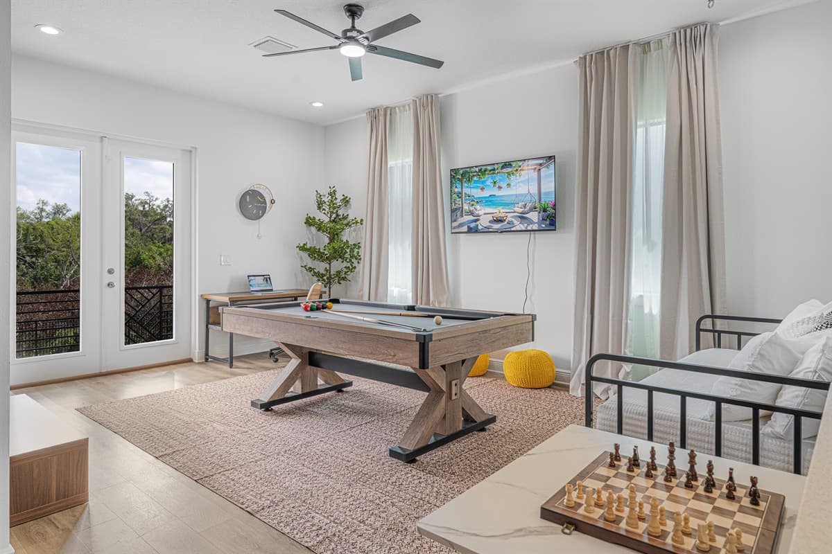 Bright game room featuring a pool table, wall-mounted TV, and large windows bringing in natural light.