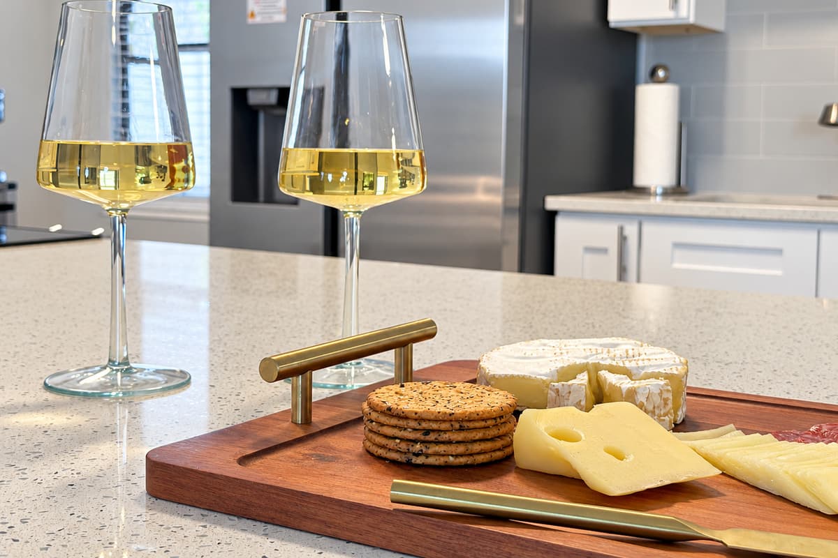 Wine glasses are already in the cabinet. Cheese board on the counter, cold glass in hand, someone still swimming out back — this is the hour between the pool and dinner that the whole day quietly builds toward.