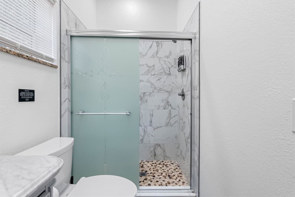 This beautifully updated bathroom features a modern walk-in shower with sleek glass doors, marble-style tile walls, and a pebble stone shower floor for a spa-like feel.