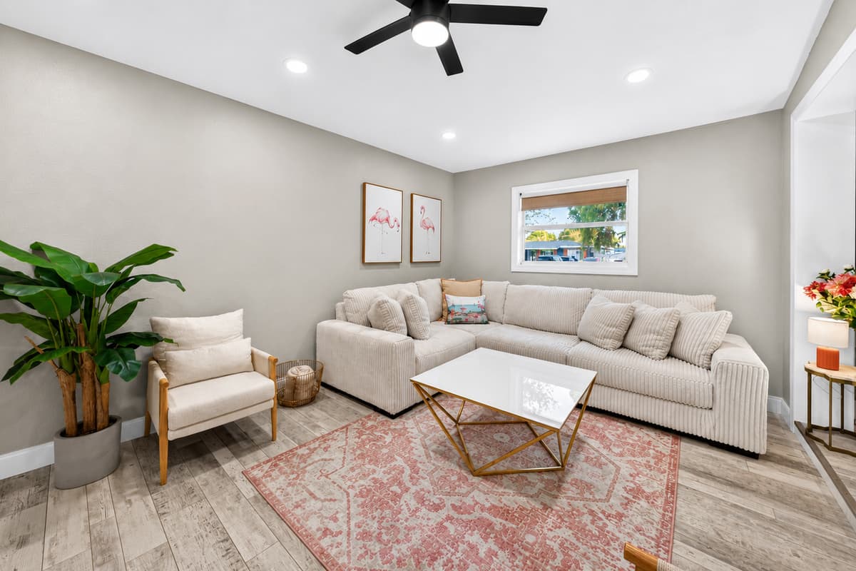 Living room corner view showing sectional sofa, accent chair, indoor plants, and soft coastal décor.