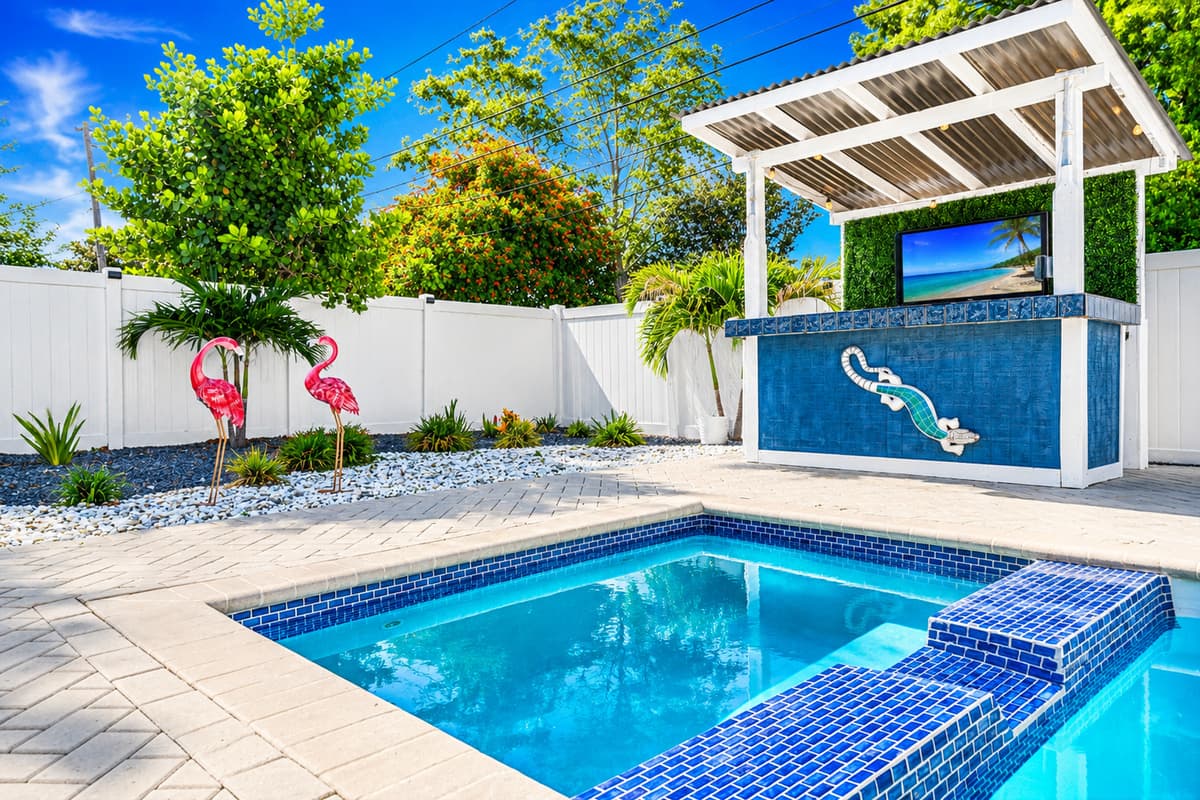 Resort-style backyard featuring a pool, raised spa, flamingo lawn décor, and covered outdoor TV bar.