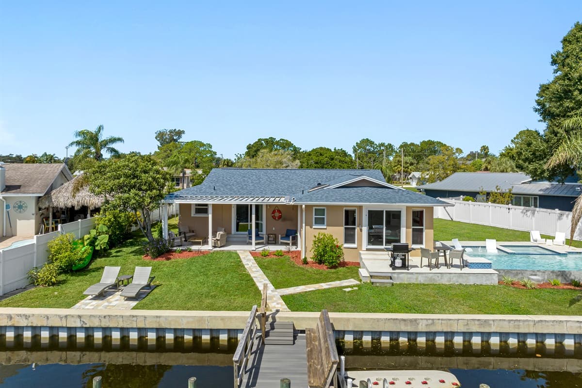 The beautiful back view of this amazing property, showcasing the wonderful swimming pool, access to dock, and the lovely patio area. Make the most of your stay! Book now!