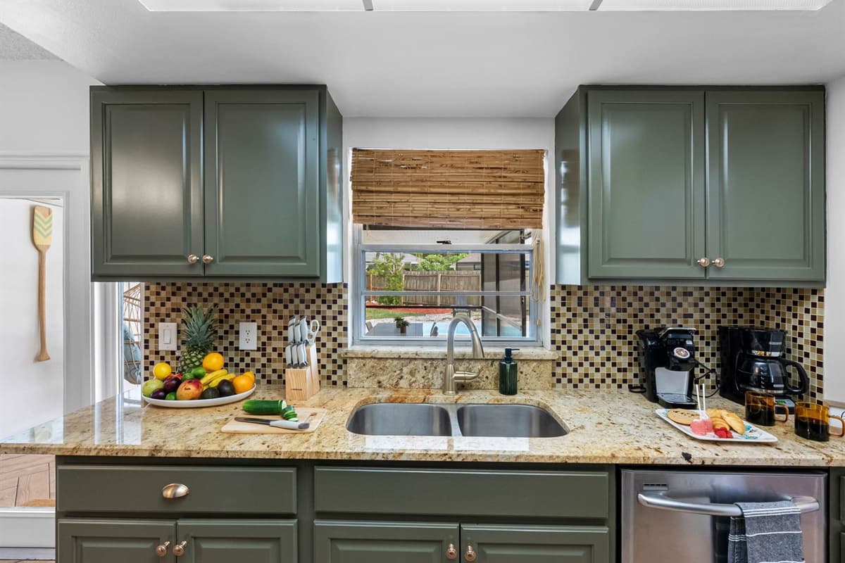 This well-equipped kitchen features sleek green cabinetry, granite countertops, stainless steel appliances, and a beautiful mosaic backsplash—ready for everything from quick breakfasts to home-cooked dinners.