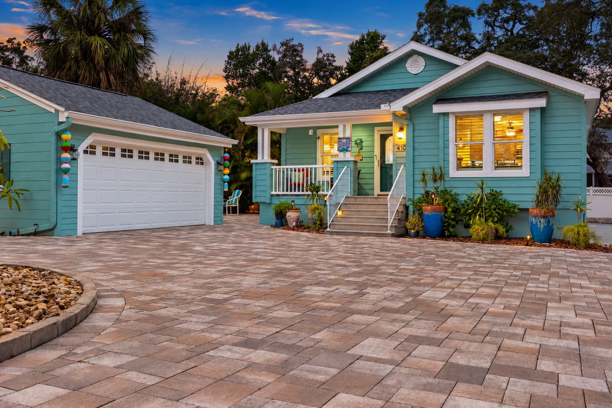 This home’s exterior blends tropical landscaping with a soft teal color scheme and a spacious, clean driveway.