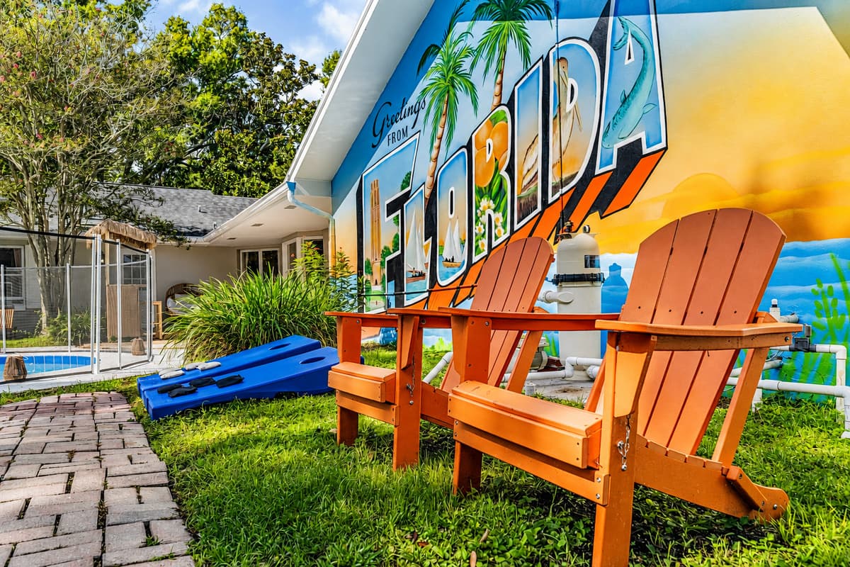 Four Adirondack chairs facing the mural, grass underfoot, shade overhead. The slow corner of the yard.