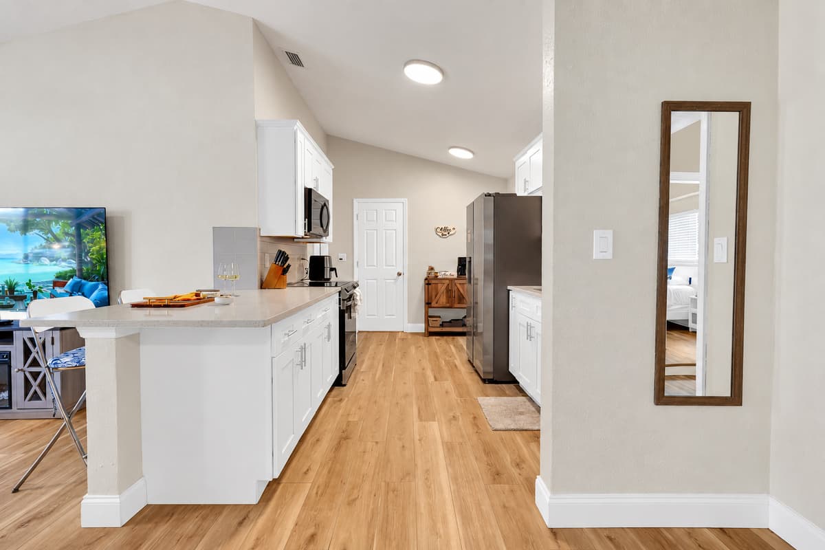 Counter runs straight toward the hallway, so groceries land once and stay put. Open sightlines from the kitchen to the living room mean whoever's cooking still hears every word of whatever is being argued about.