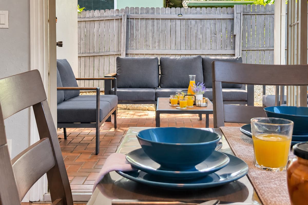 An outdoor living room, not just patio furniture. Full sofa seating under cover, the grill on one side and the pool on the other — so the group can cook, swim and sit around talking without ever having to split up.
